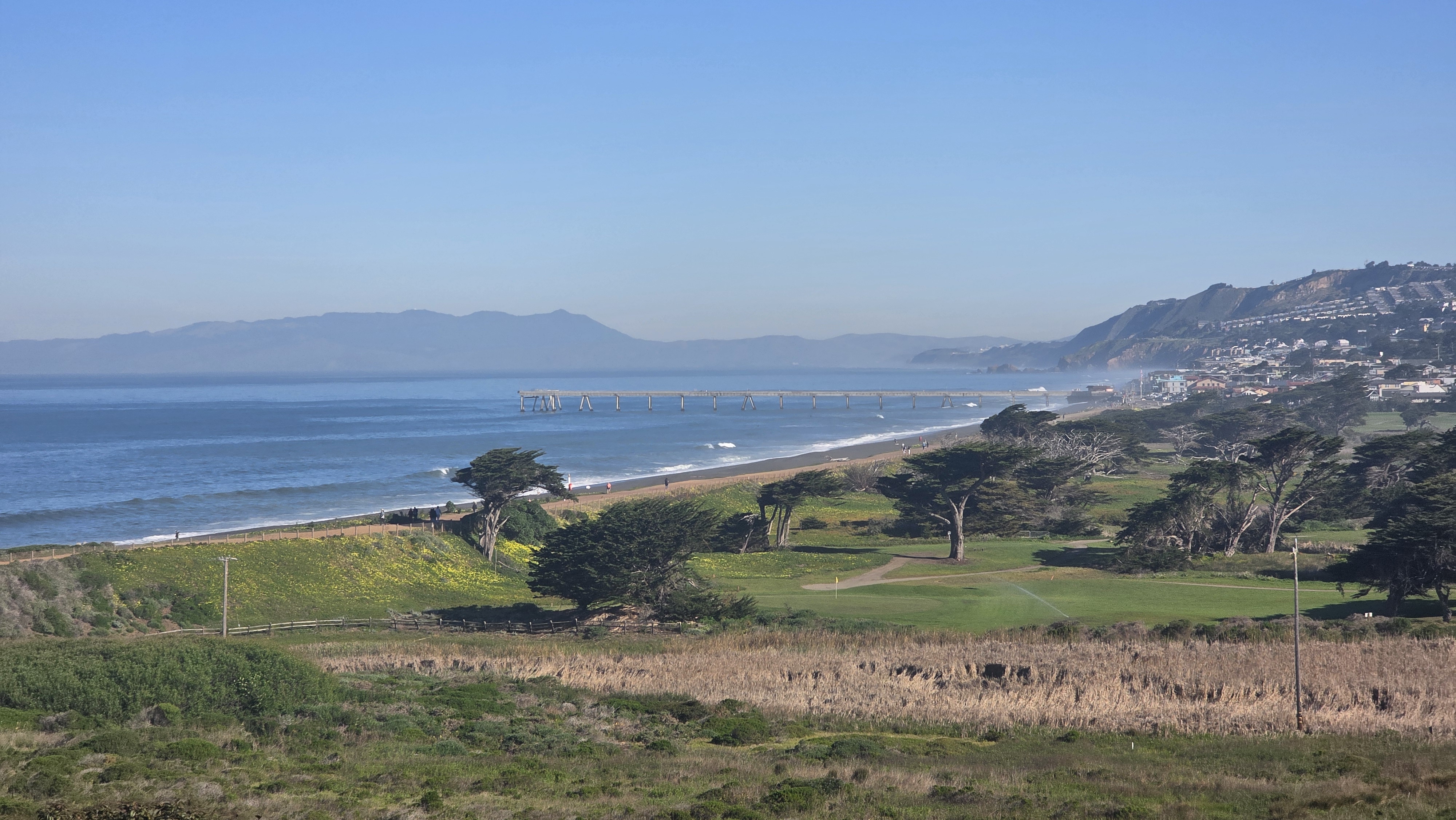 Aerial view of the Pacifica Pier, golf course, and coastline with Marin headlands in the distance